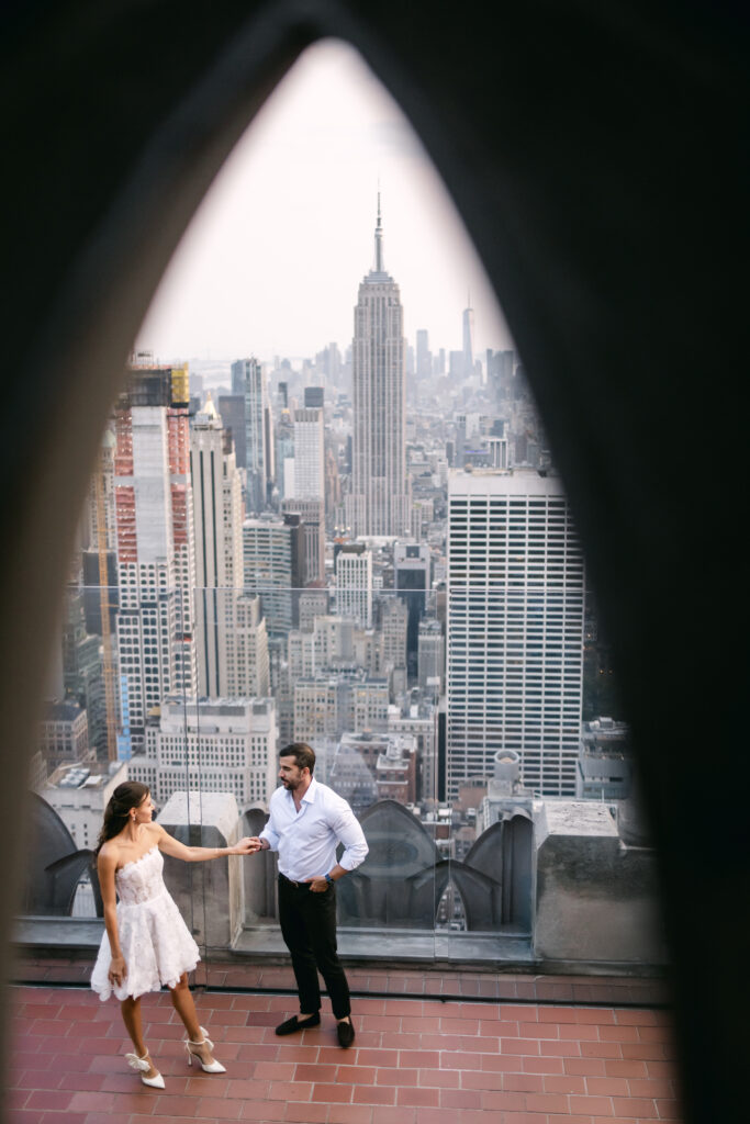 Wide shot of Olya and Felipe posing in front of the full New York City skyline at Top of the Rock during a sunset couple’s session.