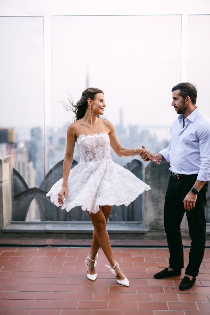 Felipe twirls Olya in a playful dance, surrounded by the dreamy NYC skyline at sunset.