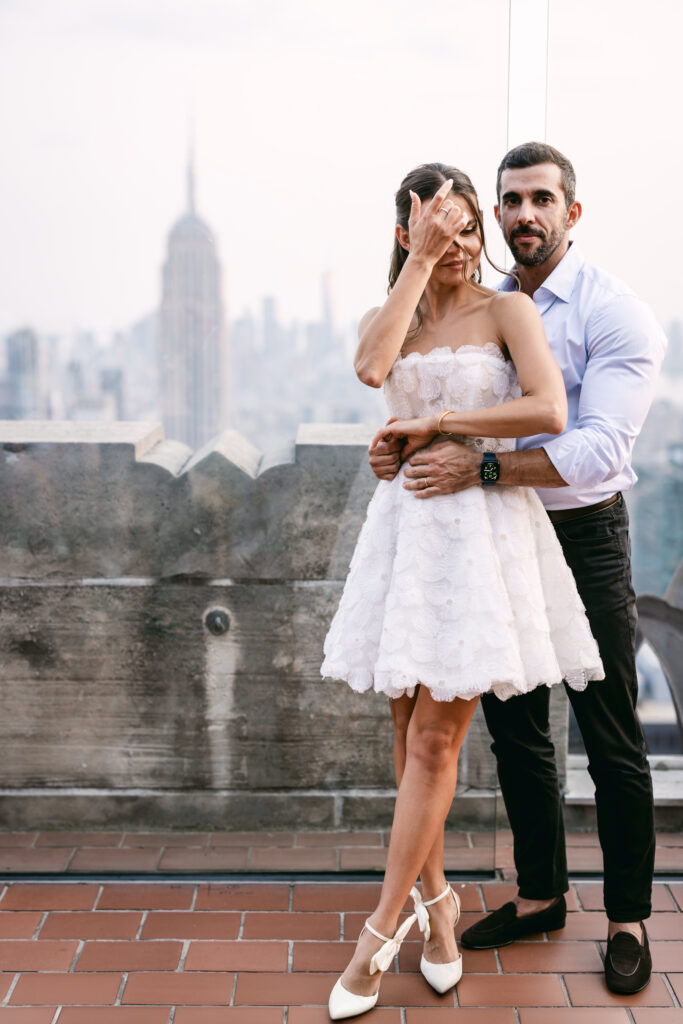 Candid moment of Felipe holding Olya's waist as she pushes her hair back during their couple's shoot at Top of the Rock, Rockefeller Center.