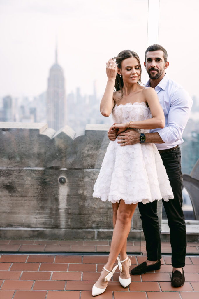 Felipe holds Olya’s waist as she pushes her hair back, bathed in the soft glow of sunset at Top of the Rock.