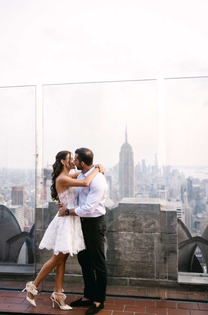 Olya and Felipe standing in front of the iconic New York City skyline at Top of the Rock, Rockefeller Center.